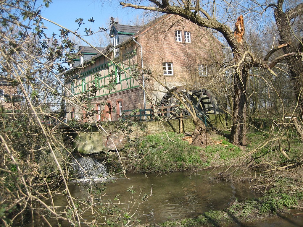 Gymnicher Mühle mit Mühlrad (2007). Vor der Mühle sind das Wehr und ein Teich zu erkennen. Links und rechts befinden sich Bäume.