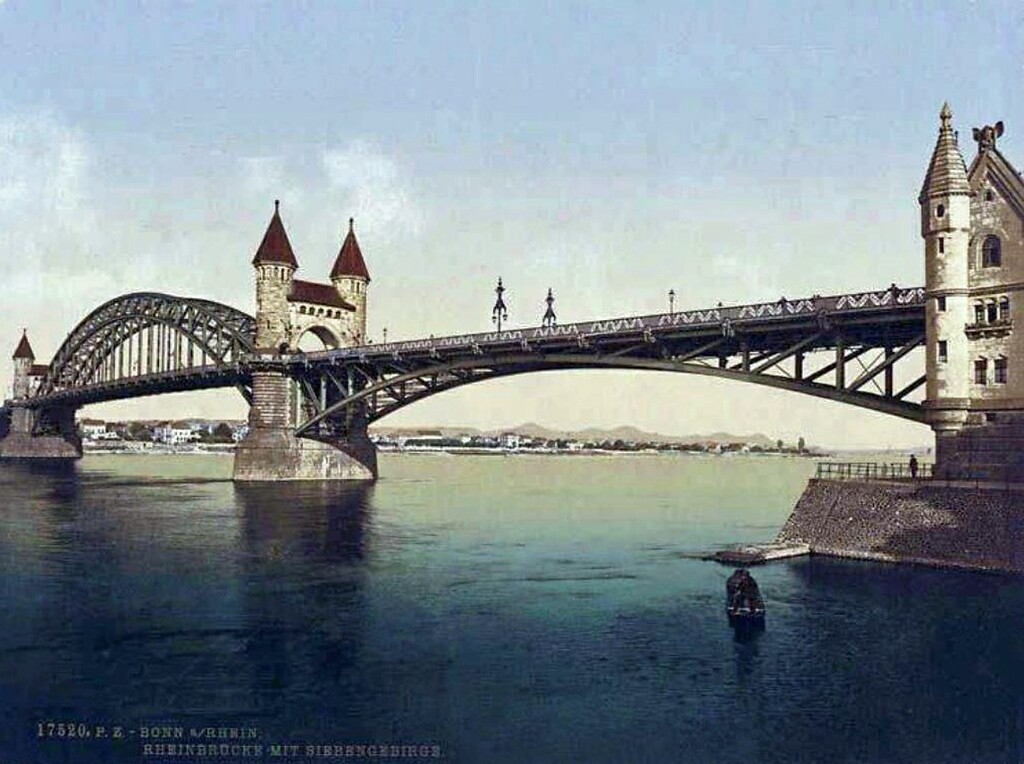Die undatierte Farbpostkarte "Bonn a/Rhein, Rheinbrücke mit Siebengebirge" zeigt die Alte Rheinbrücke vom Bonner Flussufer aus.