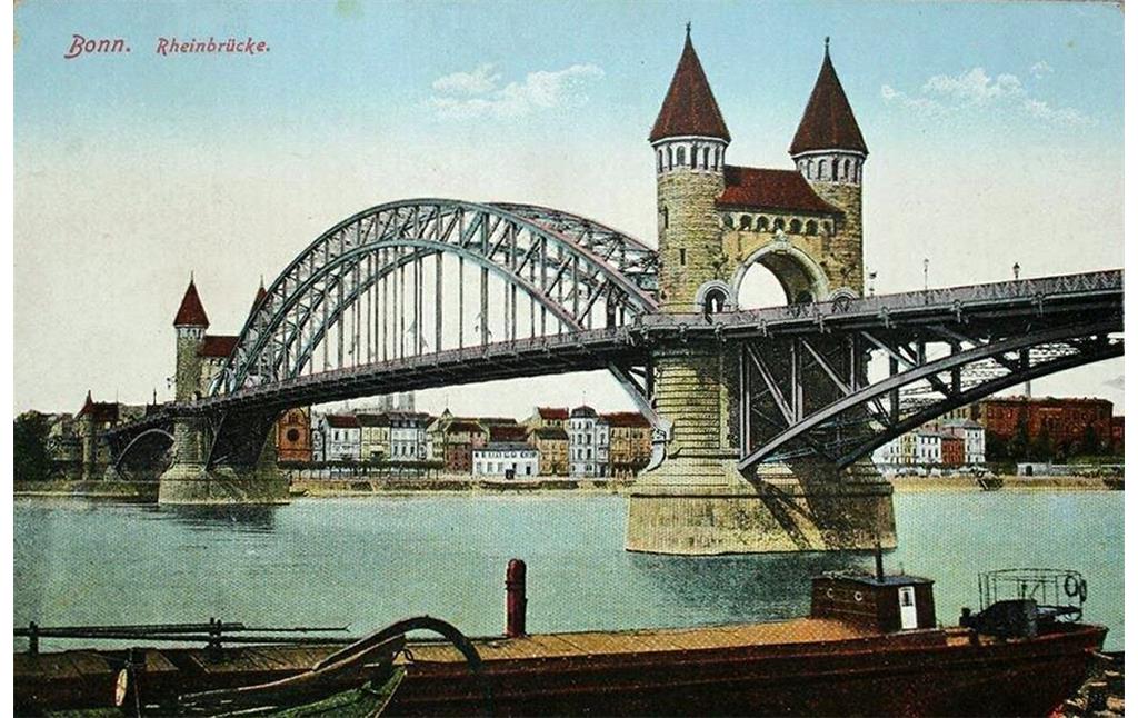 Die auf das Jahr 1918 datierte Farbpostkarte "Bonn. Rheinbrücke" zeigt die Alte Rheinbrücke vom Beueler Flussufer aus. Unter dem zentralen Brückenabschnitt ist am Bonner Rheinufer die Alte Synagoge und daneben das Hotel Dissmann zu erkennen.