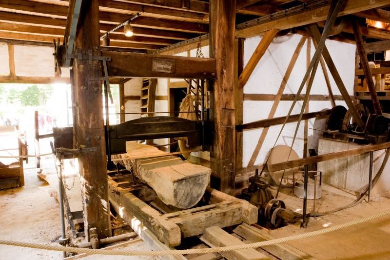 Sägegatter der Gaderother Mühle: Die Transmissionsriemen kommen von rechts oben und führen in die Bildmitte zum Sägegatter, wo ein halber Baumstamm waagerecht liegend in Bretter zersägt wird (2011).