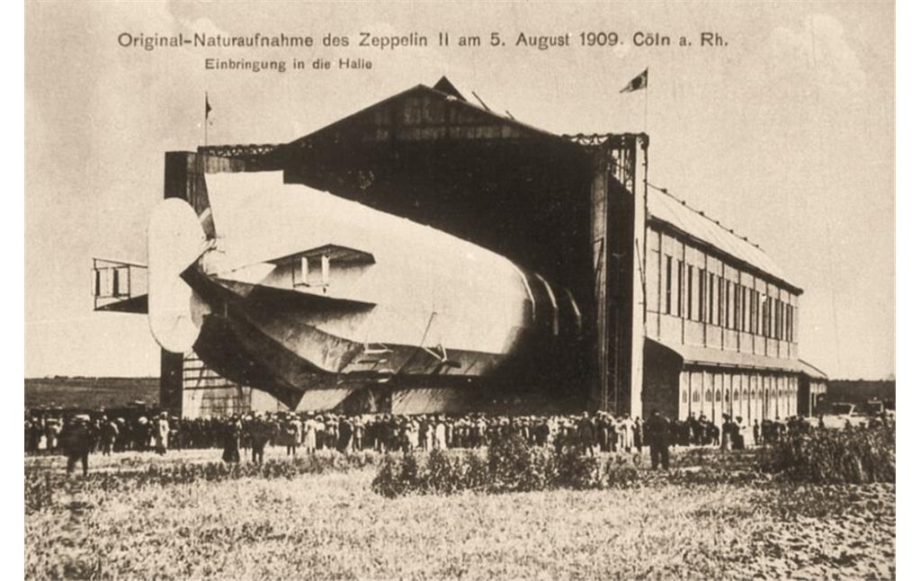 Historische Aufnahme des Kölner Luftschiffhafens von 1909: Nach seiner Landung in Bickendorf wird das 136 Meter lange Luftschiff LZ 5 / Z II in die Luftschiffhalle verbracht.