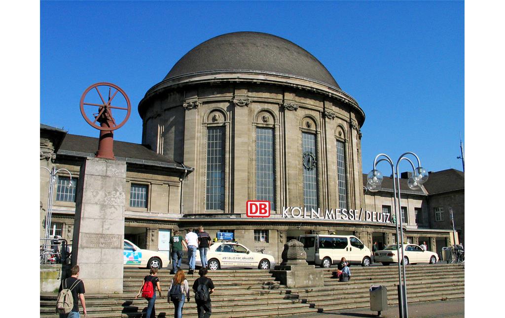 Das Empfangsgebäude des Bahnhofs Köln Messe/Deutz, links das Denkmal für Nikolaus August Otto auf dem Ottoplatz (2005).