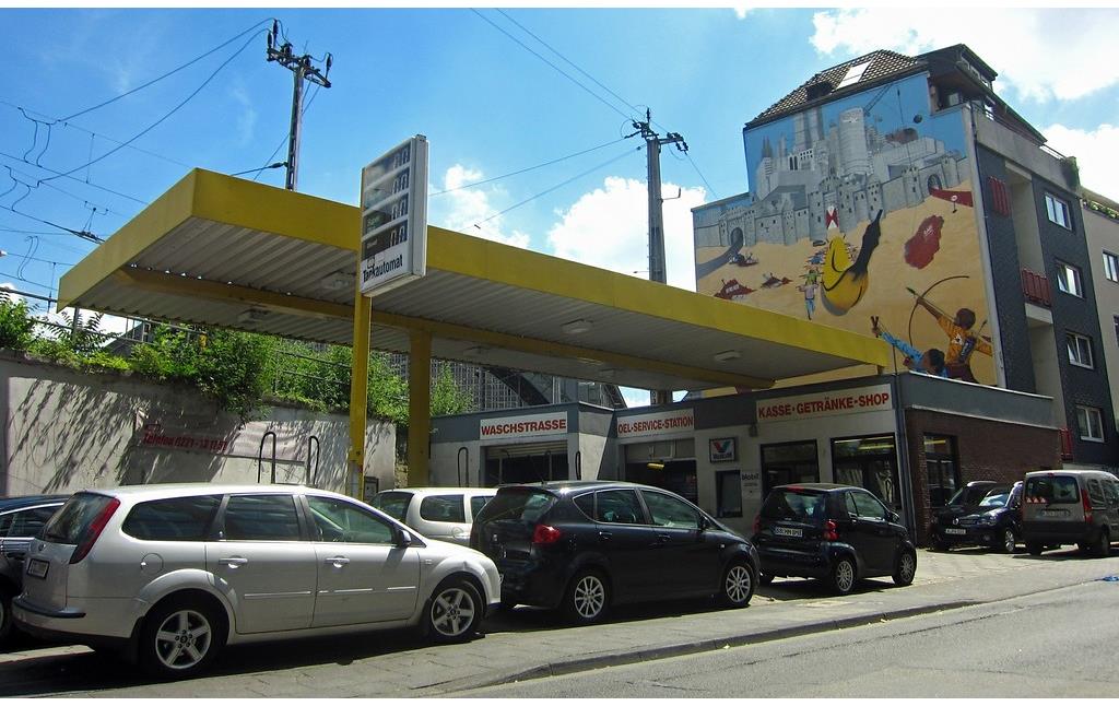 Die ehemalige Tankstelle in der Kölner Marzellenstraße, die heute als KFZ-Service und Waschanlage betrieben wird (2015). Die Fassade des Hauses dahinter ist durch ein großformatiges Graffiti gestaltet.