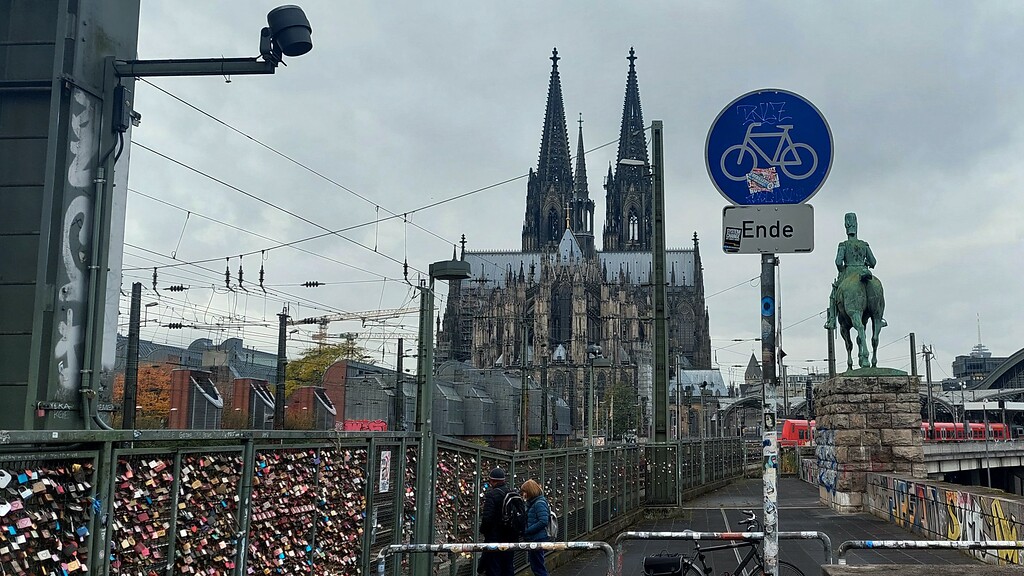 Blick von der Kölner Hohenzollernbrücke auf Liebesschlösser am nördlichen Geh- und Radweg, dahinter der Dom und das Reiterstandbild von Kaiser Friedrich III. (2021).