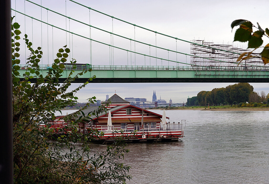 Blick in Richtung des Kölner Doms und die Rodenkirchener Autobahnbrücke in Köln-Rodenkirchen (2021). Im Vordergrund auf dem Wasser ist das Lokal "Alte Liebe" zu sehen.