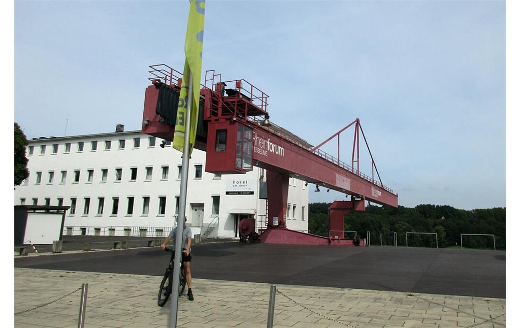 Historischer Hafenkran am Platz-am-Rheinforum in Wesseling, dahinter ein Gebäude des "Hotel am Rhein" (2023).