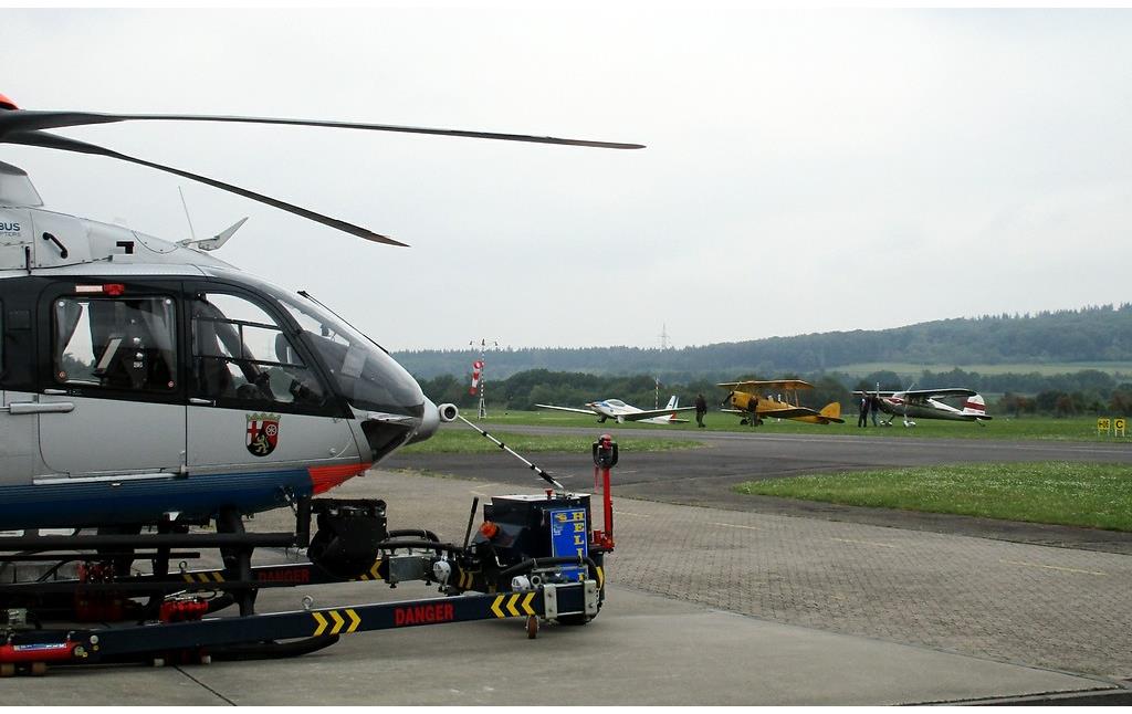 Der Flugplatz Koblenz-Winningen dient auch als Sitz der Polizeihubschrauberstaffel Rheinland-Pfalz: im Vordergrund der Polizeihubschrauber "Sperber" D-HRPB (Typ Eurocopter EC 135), dahinter Sportflugzeuge (2016).