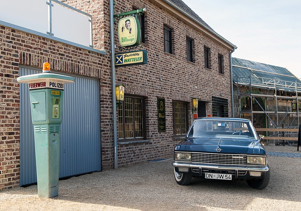 Der "Marktplatz Rheinland" im LVR-Freilichtmuseum Kommern (2022). Im Bild die Gaststätte Watteler im Stil der 1950/70er-Jahre, davor eine zeittypische Notrufsäule und ein Opel der 1964-1968 produzierten Baureihe KAD (Serie A).
