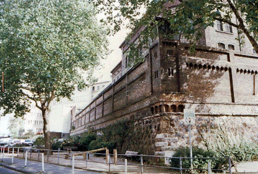 Blick auf die Bastionsmauer der Justizvollzugsanstalt Bonn an der Ecke Annagraben / Alexanderstraße (vor 1995). Unter dem als Eckrisalit ausgeführten Wachttürmchen ist eine barocke Kartusche mit kurfürstlichem Wappen in die Mauer eingelassen.