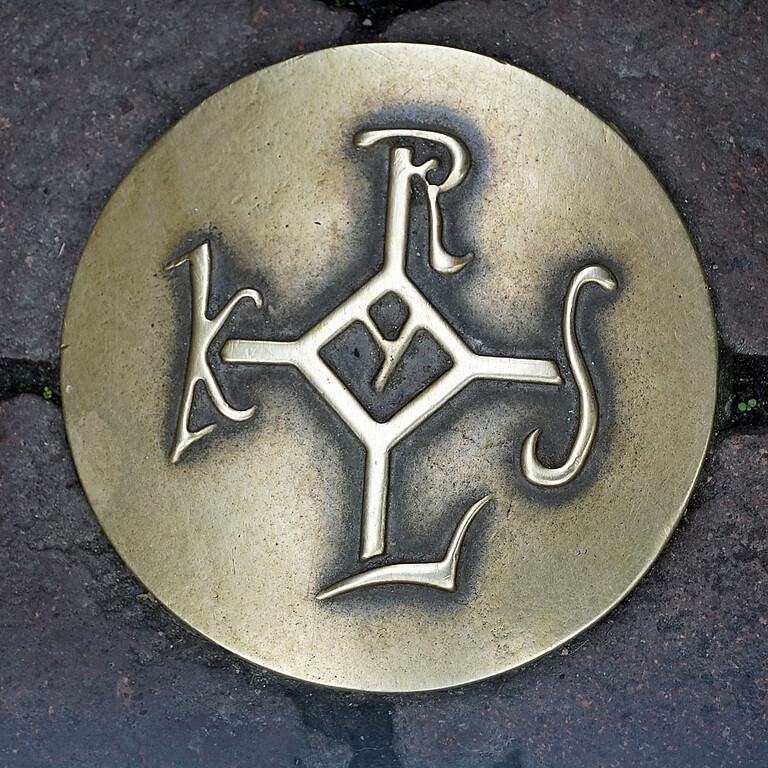 Bronzenes Karolus-Monogramm, auch Karlsmonogramm, als Wegweiser eines Kulturpfades in Aachen-Mitte 2021). Das vorgeschriebene Signum diente als die Unterschrift des Kaisers, welche er mit dem sogenannten Vollziehungsstrich vollendete.