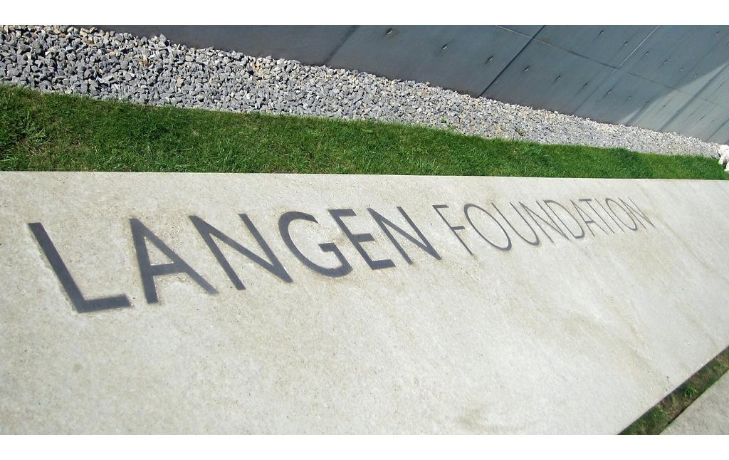 Eine Bank mit der Aufschrift "Langen Foundation" vor dem Eingang der Kunst-und Ausstellungshalle der Langen Foundation (2014)