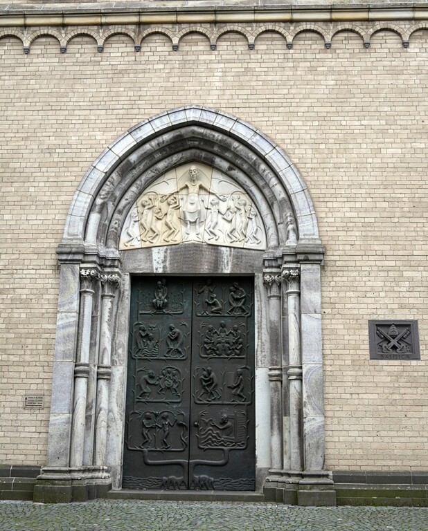 Das von dem Kölner Bildhauer Elmar Hillebrand (1925-2016) gestaltete nördliche Portal zu der Kirche des Kunibertstifts in Köln-Altstadt-Nord (2023). Rechts ist die Tafel zur "Basilica minor" zu sehen.