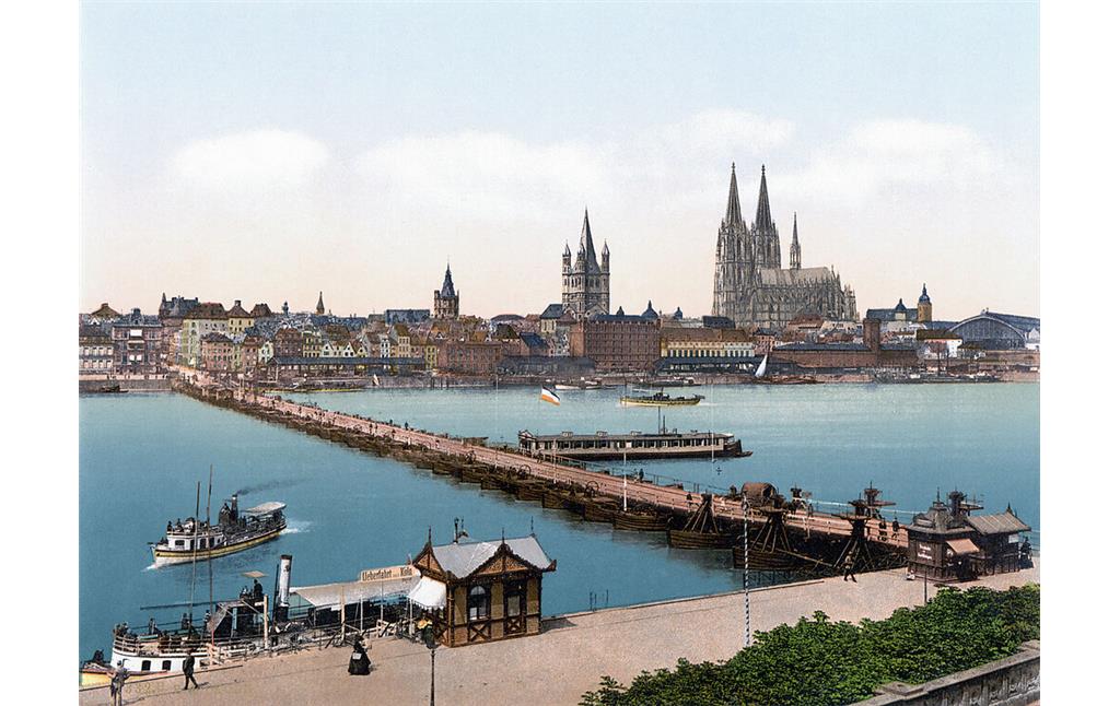 Die hölzerne Schiffsbrücke zwischen Deutz und Köln, eines der Vorgängerbauwerke der heutigen Deutzer Brücke (kolorierte Postkarte von um 1900). Im Bildvordergrund Personenfähren und mittig das an der Brücke angelegte "Badeschiff" der Flussbadeanstalt.