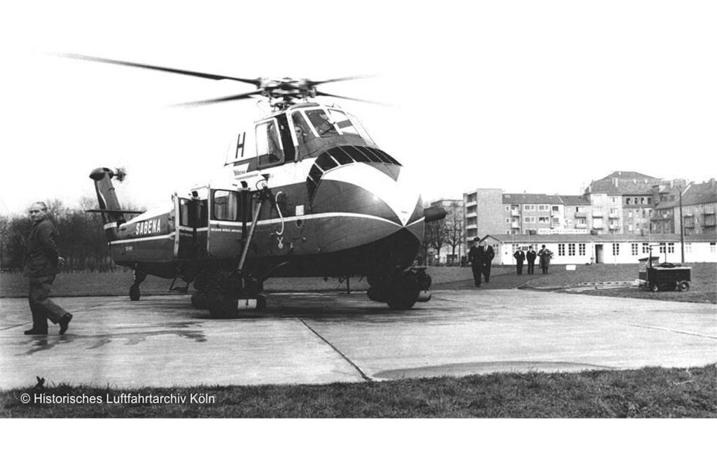 Ein im Hubschrauber-Linienflugverkehr der belgischen Fluggesellschaft Sabena eingesetzter Helikopter vom Typ Sikorsky S-58 (Aufnahme zwischen 1953 und 1958), hier auf der Landeplattform des Hubschrauberflughafens Köln, links im Bild der Chef des Kölner Heliports Franz Knapp.