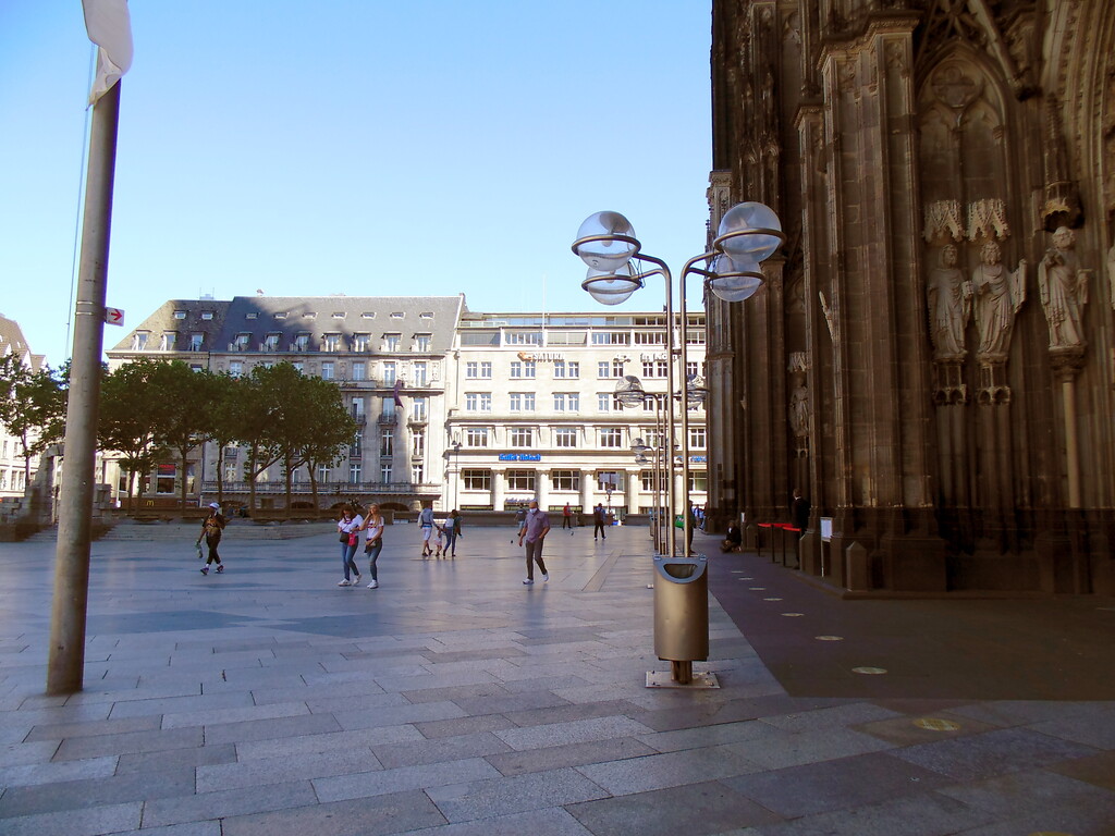 Blick von der Domplatte im Bereich der Hauptportalzone auf das im Hintergrund gelegene Deichmannhaus in der Kölner Altstadt-Nord. Links vom Deichmannhaus befindet sich das traditionsreiche Excelsior Hotel Ernst (2020).