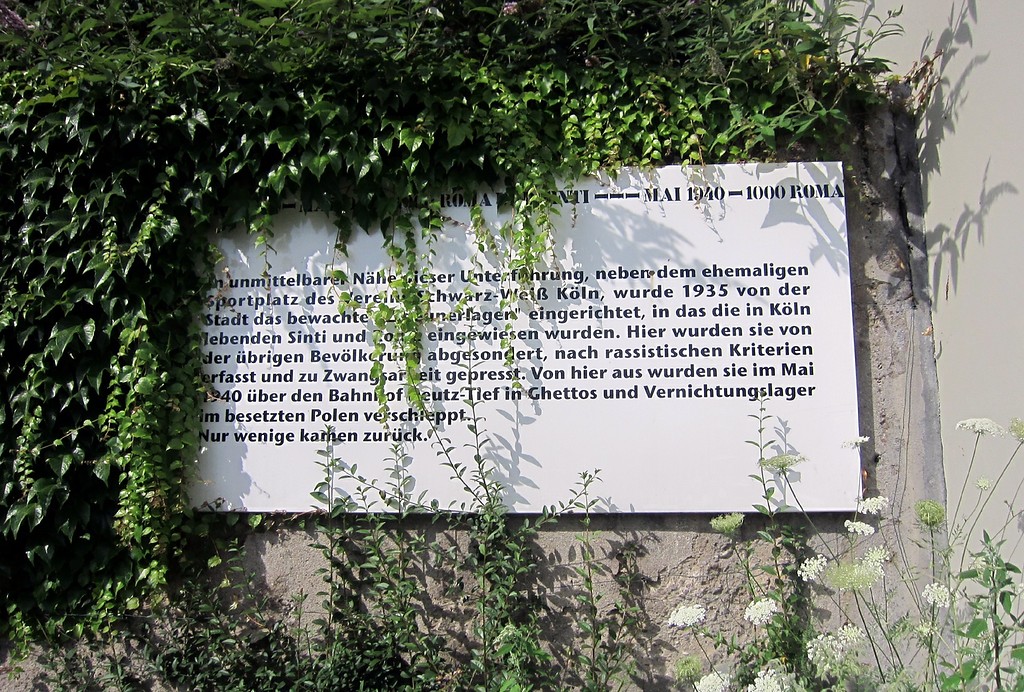 Allmählich zuwachsende Gedenktafel für das so genannte "Zigeunerlager" an der Eisenbahnbrücke Venloer Straße in Köln-Bickendorf (2013)