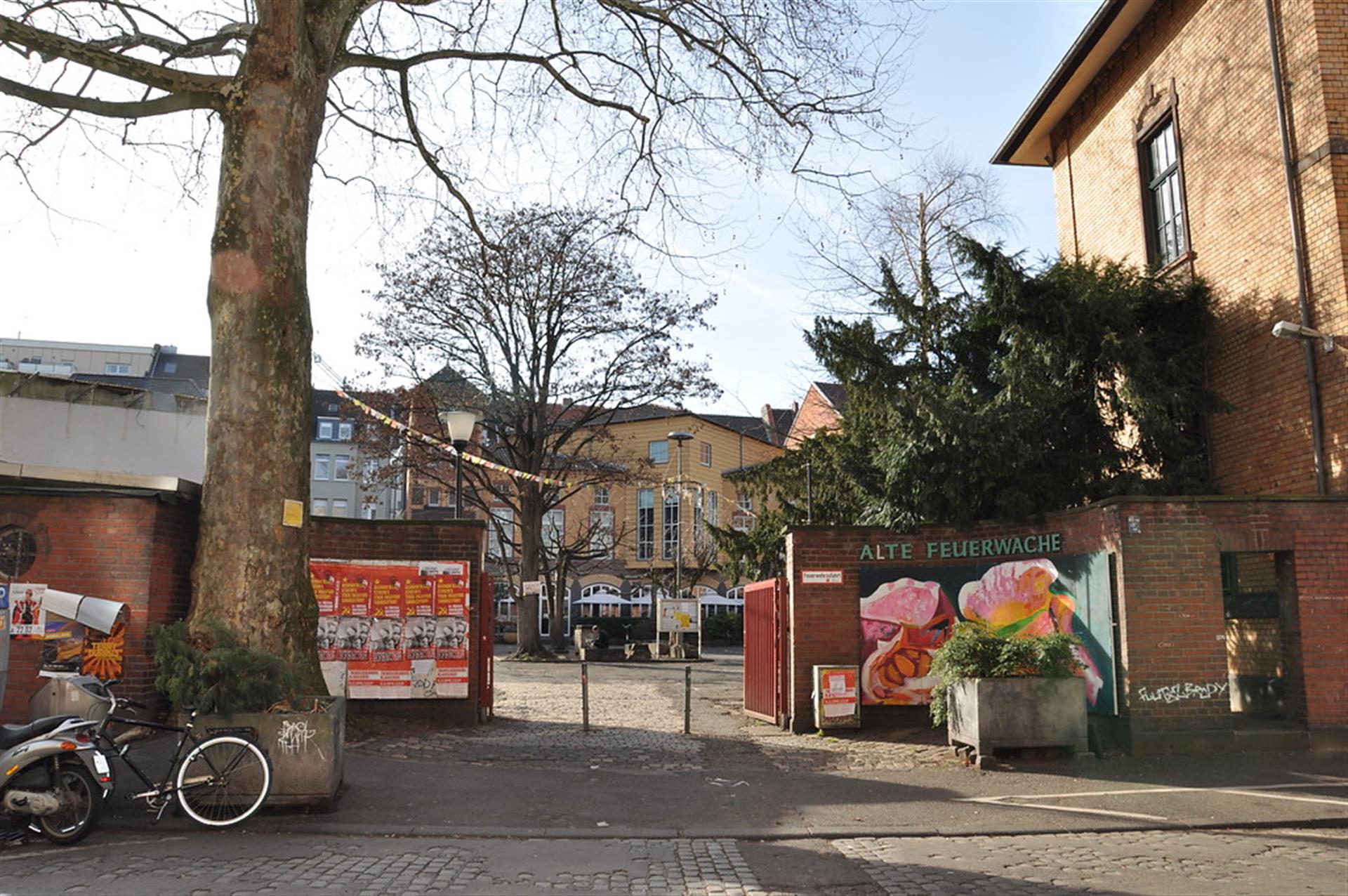 Das Bild zeigt das Bürgerzentrum Alte Feuerwache von der Melchiorstraße aus gesehen. In der Mitte des Bildes befindet sich das Tor der Feuerwache, innerhalb dessen zwei Poller stehen, da die Befahrung des Hofes mit Fahrzeugen verboten ist. Rechts neben dem Tor steht die Aufschrift "Alte Feuerwache". &copy; null