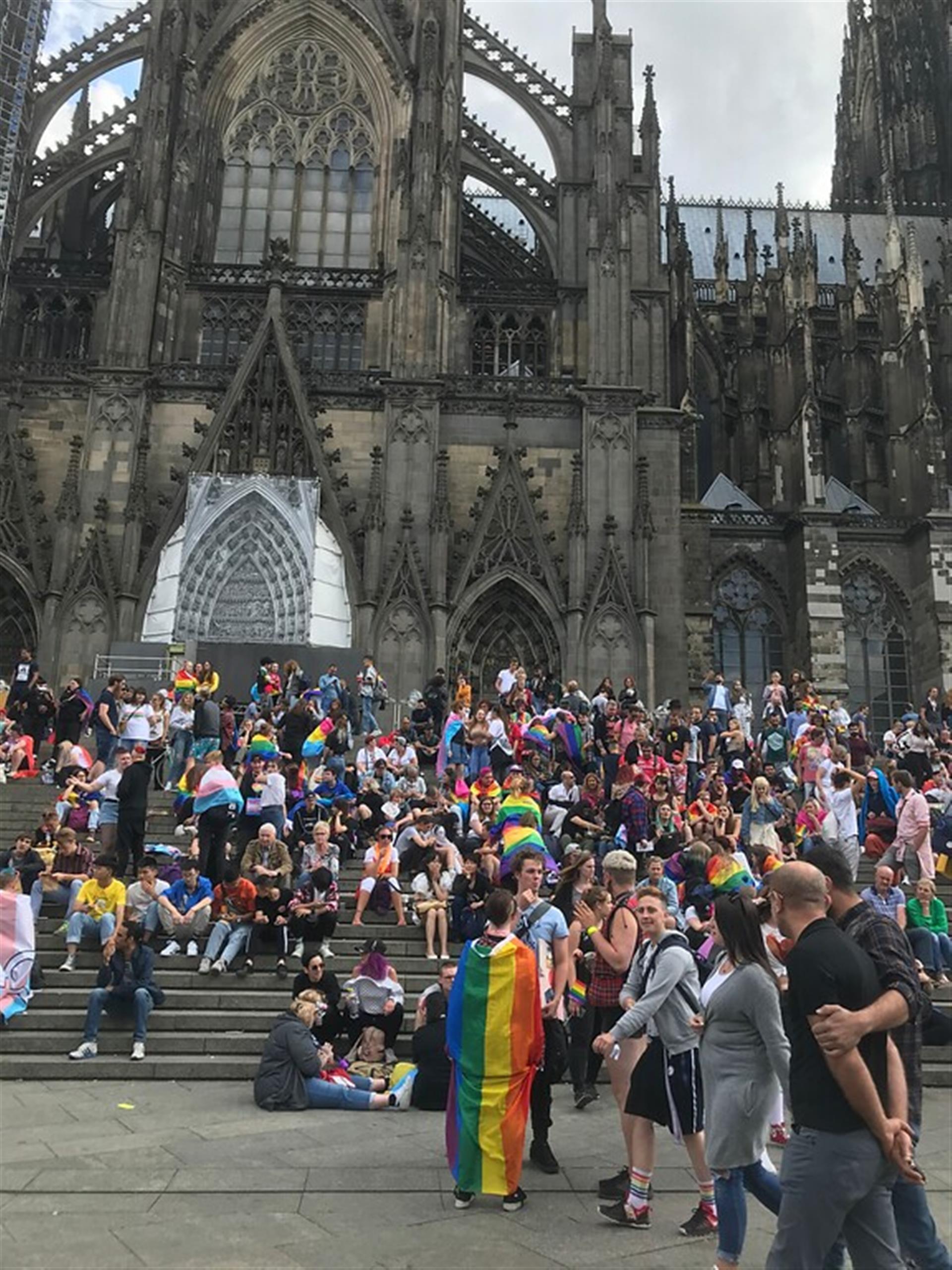 Der Christopher-Street-Day in Köln-Innenstadt (2019); auf den Treppen zum Kölner Dom versammeln sich hunderte Feiernde, viele davon mit Fahnen in verschiedenen Pride-Farben. &copy; Janina Schwiderski / Landschaftsverband Rheinland / CC BY-4.0