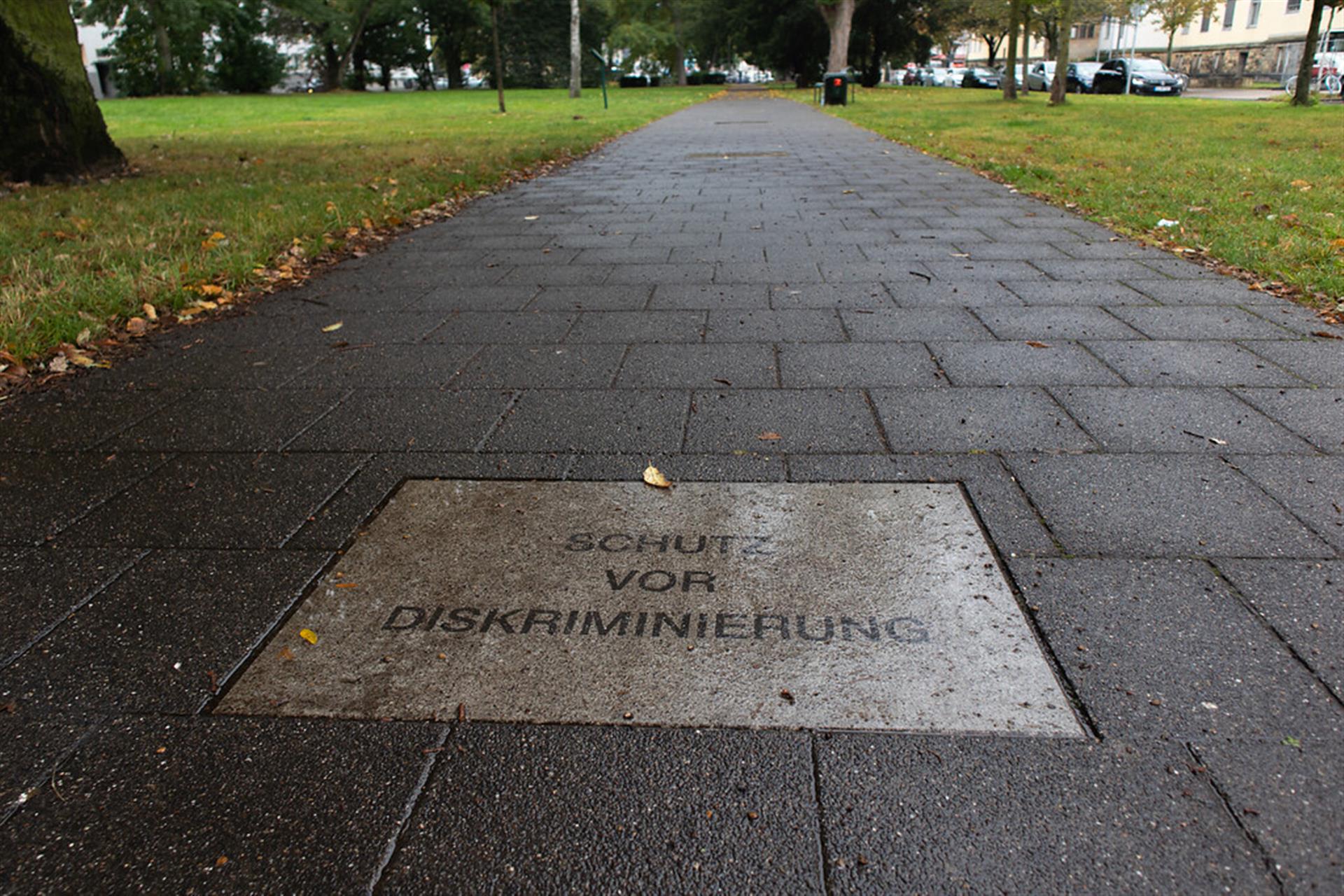 Ein Blick in den Park der Menschenrechte in Köln-Lindenthal (2021); zu sehen sind ein Gehweg und die Bodenplatte mit der Inschrift "Schutz vor Diskriminierung". &copy; Janina Schwiderski / Landschaftsverband Rheinland / CC BY 4.0