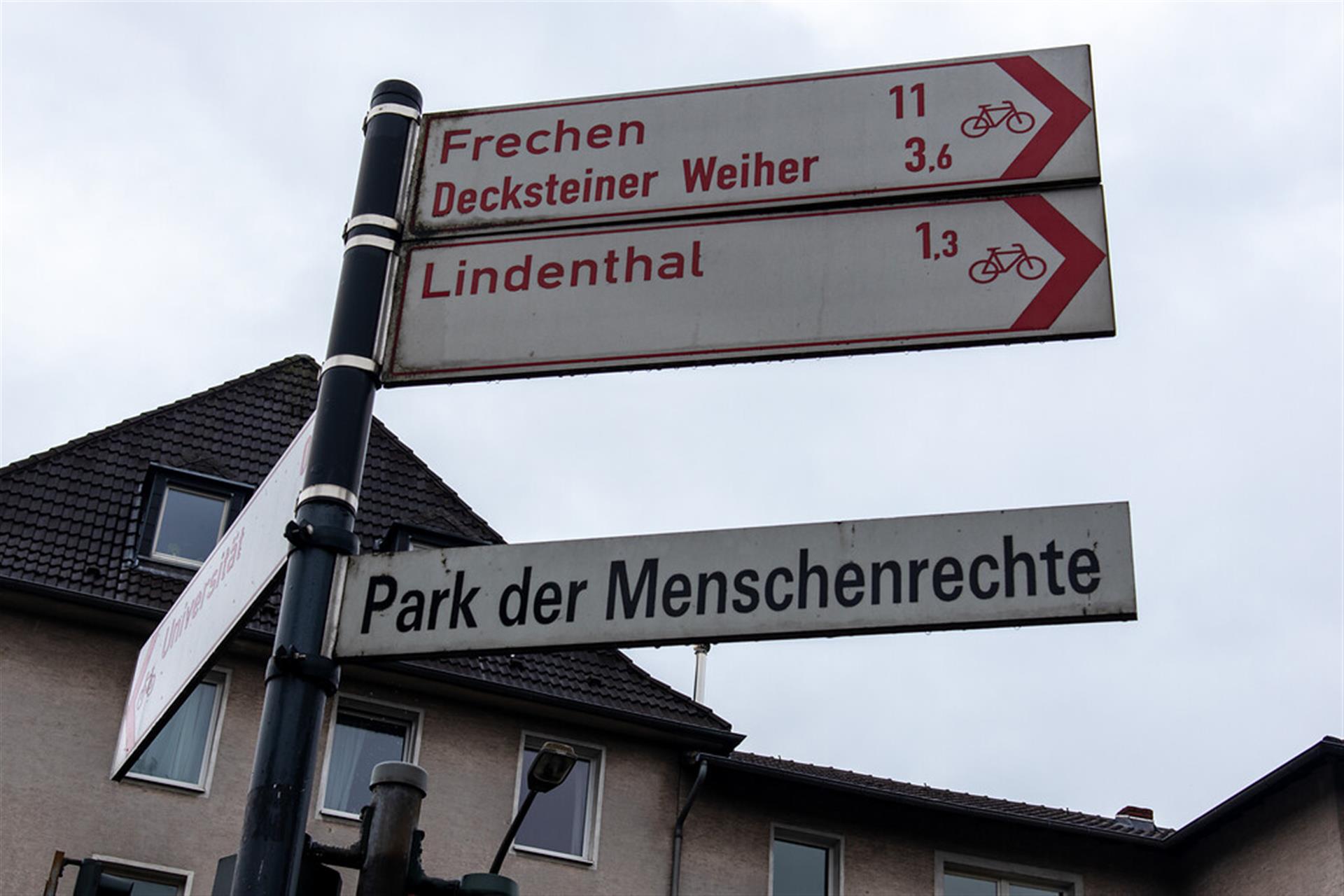 Das Straßenschild "Park der Menschenrechte" am Eingang des Parks befindet sich unter den Entfernungshinweisen für die Fahrradstrecken nach Lindenthal und Frechen zum Decksteiner Weiher. &copy; Janina Schwiderski / Landschaftsverband Rheinland / CC BY 4.0