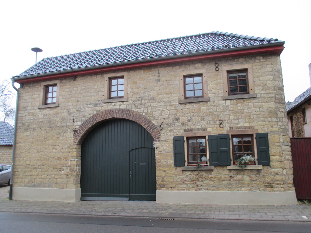Dieses Bruchsteinhaus in Bürvenich weist ein großes Hoftor mit Fußgängertür und aus Backstein gemauertem Rundbogen auf. Die Anker bilden die Jahreszahl 1868. (2014)