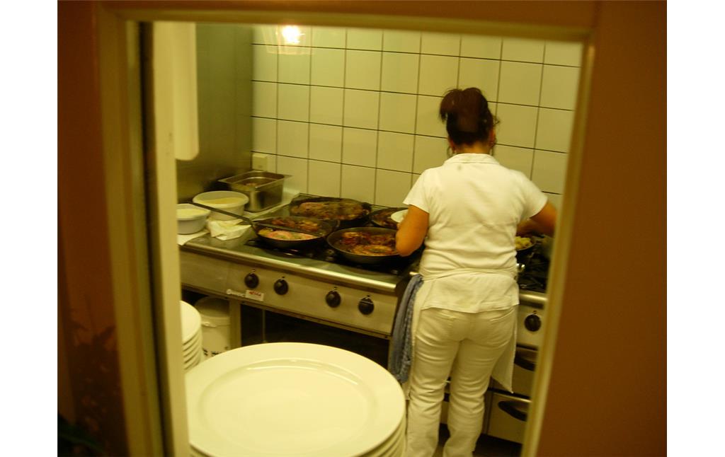 Die Küche der Gaststätte Lommerzheim (2008). Eine Frau bereitet in großen Stahlpfannen Essen zu.