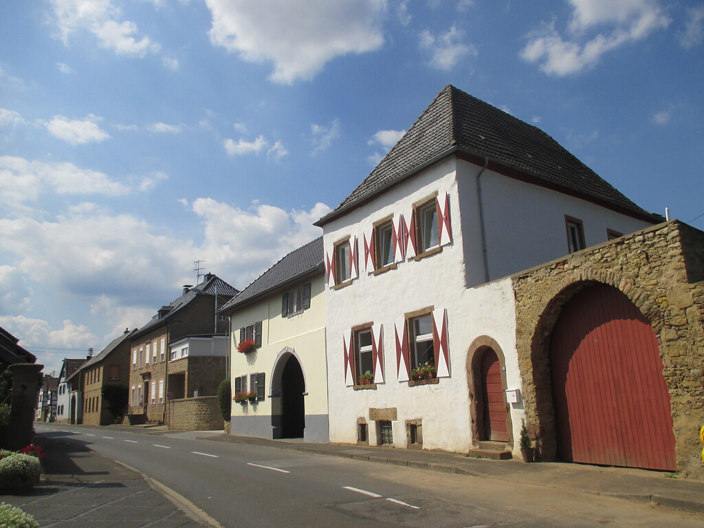 Straßenzeile in Embken mit weiß gestrichenem Herrenhaus eines ehemaligen Gutshofes und Hofmauer mit Rundbogentor und Fußgängerpforte (2015)