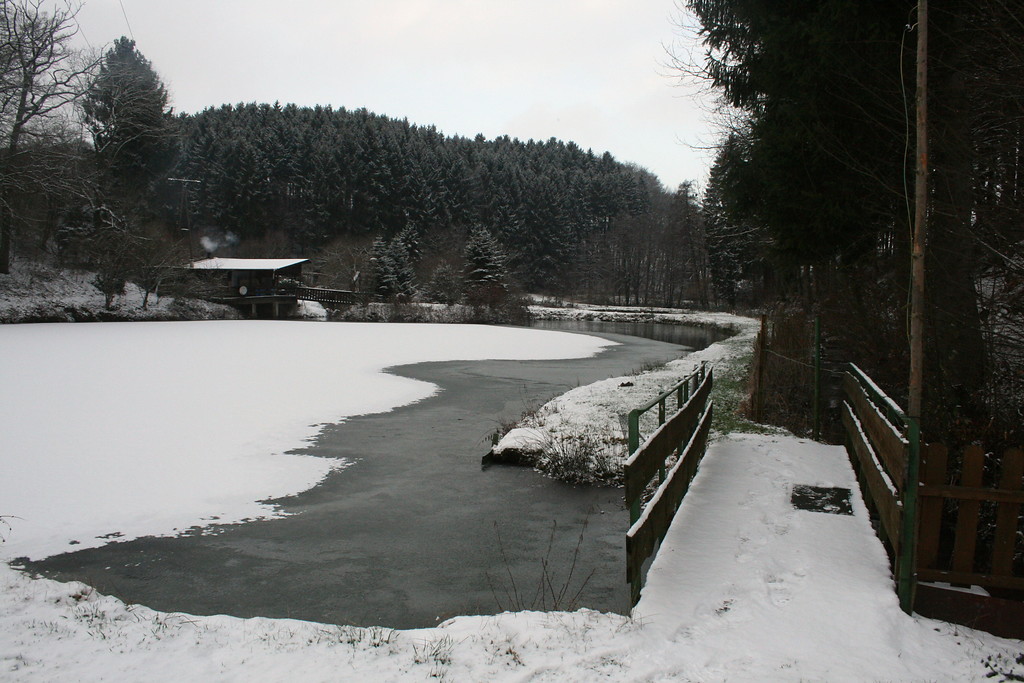 Blick vom Damm über den zugefrorenen Stauteich; rechts der Ablauf mit dem Grundablass.