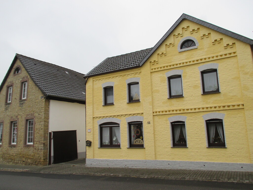 Im Straßendorf Bürvenich steht dieses Bruchsteinhaus neben einem gelb gestrichenen Backsteinhaus mit geometrischen Verzierungen. (2014)