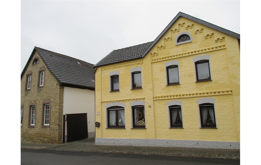 Im Straßendorf Bürvenich steht dieses Bruchsteinhaus neben einem gelb gestrichenen Backsteinhaus mit geometrischen Verzierungen. (2014)