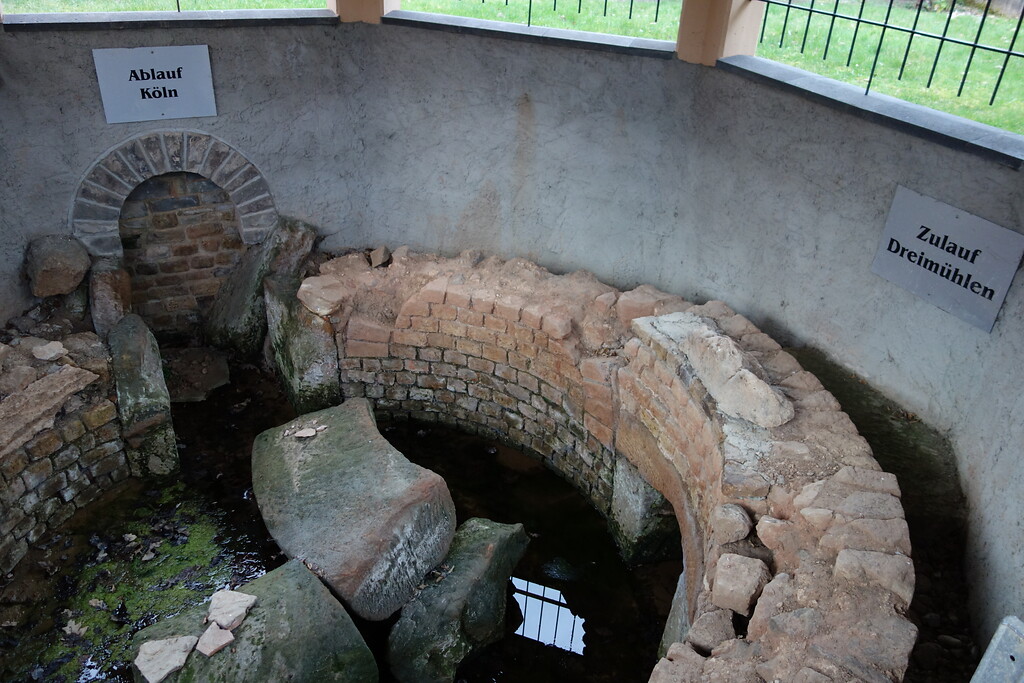 Das rund gemauerte römische Sammelbecken in Eiserfey sammelte die Wässer aus den Richtungen Kallmuth, Urfey und Dreimühlen. Die entsprechenden Zulaufkanäle sind mit Tafeln beschriftet. Das Wasser verließ das Sammelbecken durch einen zentralen Ablauf Richtung Köln (im Bild links) (2020).