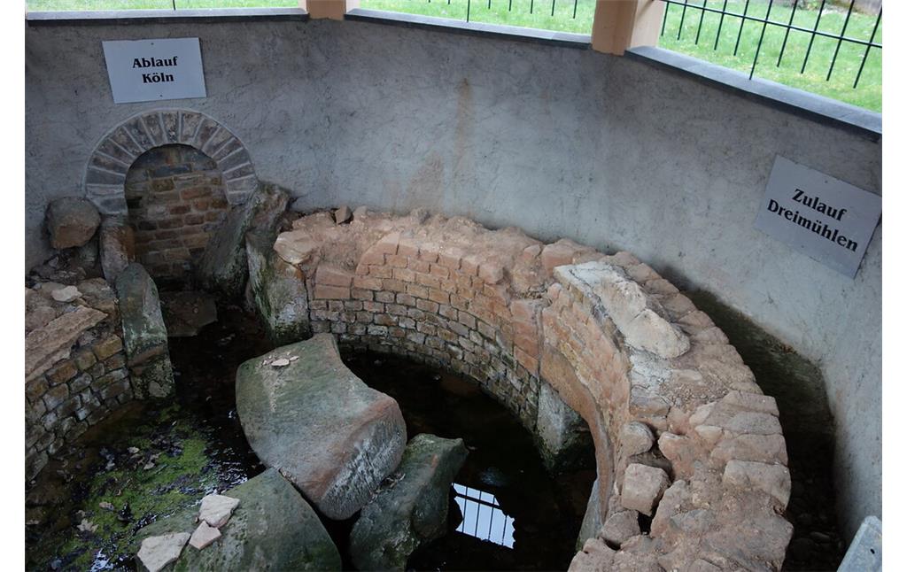 Das rund gemauerte römische Sammelbecken in Eiserfey sammelte die Wässer aus den Richtungen Kallmuth, Urfey und Dreimühlen. Die entsprechenden Zulaufkanäle sind mit Tafeln beschriftet. Das Wasser verließ das Sammelbecken durch einen zentralen Ablauf Richtung Köln (im Bild links) (2020).