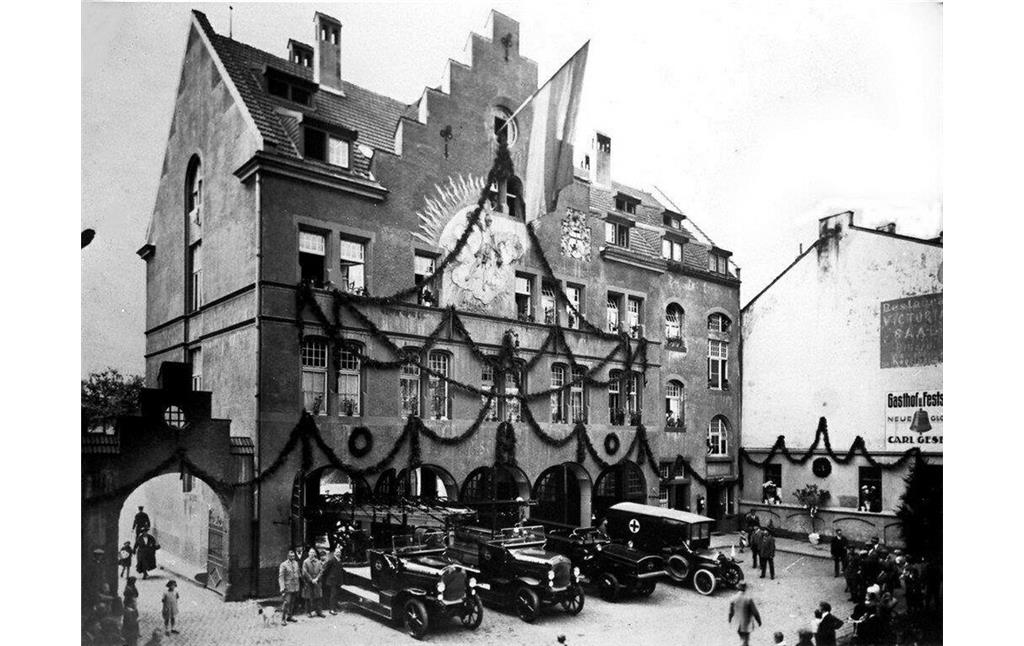 Historische Aufnahme der festlich geschmückten Alten Feuerwache Bonn in der damaligen Karl-Marx-Straße (9. August 1924), davor drei Feuerwehrfahrzeuge und ein Krankenwagen.