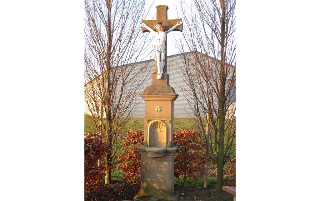 Wegekreuz an einer Weggabelung bei Füssenich. Das Rotsandsteinkreuz mit Korpus aus Stein steht auf einem untergliederten Sockel mit Nische und goldenen Verzierungen. (2015)