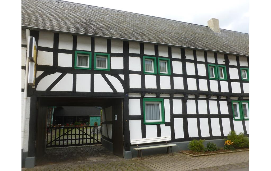 Dieses Fachwerkgebäude in Hostel weist eine Hofdurchfahrt, grün eingerahmte Holzfenster und einen verzierten Balken auf. (2014)