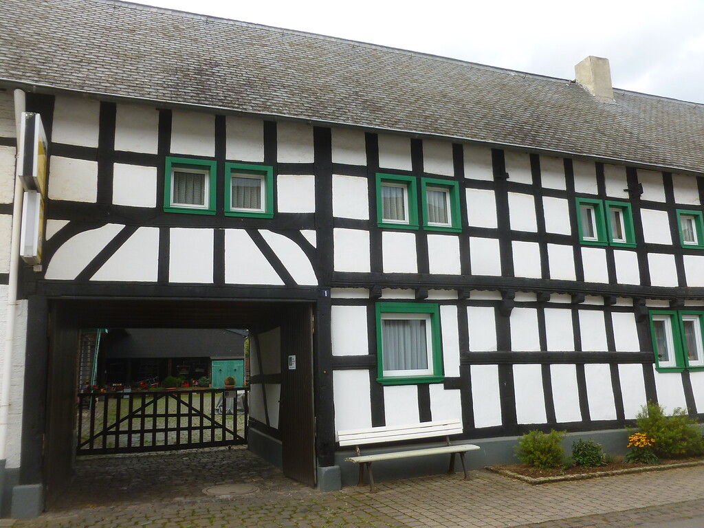 Dieses Fachwerkgebäude in Hostel weist eine Hofdurchfahrt, grün eingerahmte Holzfenster und einen verzierten Balken auf. (2014)