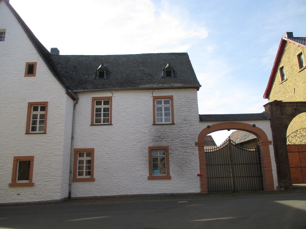 Die Burg Pissenheim ist ein weiß getünchter, vierflügeliger Bruchsteinbu mit rot gestrichenen Sandsteineinfassungen der Fenster und einem Torbogen zum Hof mit verziertem Metalltor. (2015)