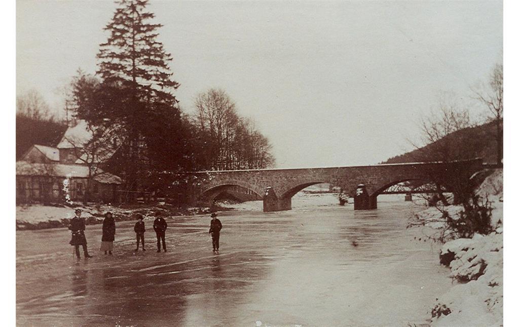 Historische Aufnahme (Ende 19./Anfang 20. Jahrhundert): Blick auf Schlittschuhfahrer auf der zugefrorenen Agger bei Engelskirchen-Loope. Im Hintergrund ist die alte Steinbrücke zu sehen.