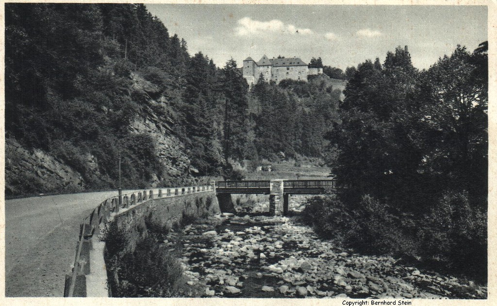 Undatierte Postkarte (wohl nach dem Ersten Weltkrieg): Die St. Vither Straße / Reichsstraße 399 in Monschau an der Rur mit Niedrigwasse, dahinter  die Burg Monschau.