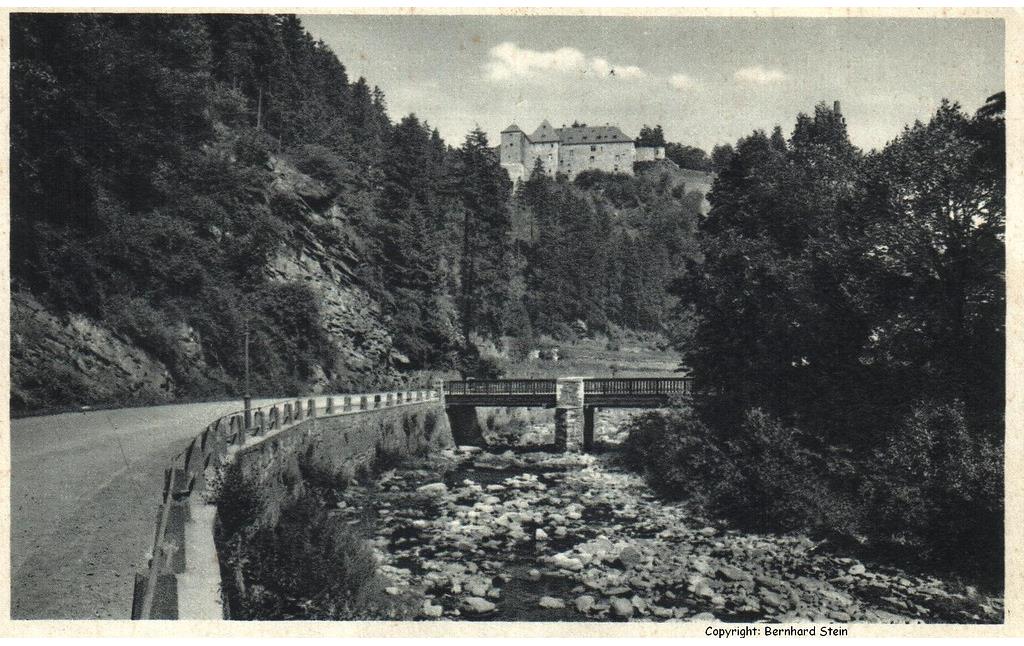 Undatierte Postkarte (wohl nach dem Ersten Weltkrieg): Die St. Vither Straße / Reichsstraße 399 in Monschau an der Rur mit Niedrigwasse, dahinter  die Burg Monschau.