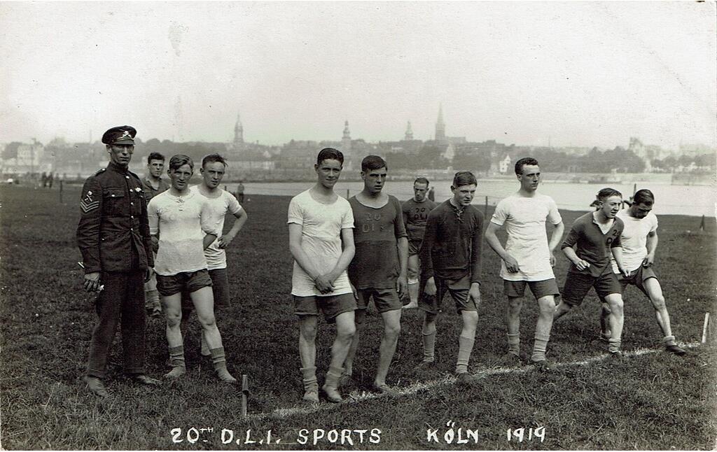 Historische Aufnahme von 1919: Englische Besatzungssoldaten treiben Sport auf den Kölner Rheinwiesen. Der Bildbeschriftung nach handelt es sich um Soldaten der "20th Division" der "Durham Light Infantry" (D.L.I.). Im Hintergrund ist Köln-Mülheim zu sehen.