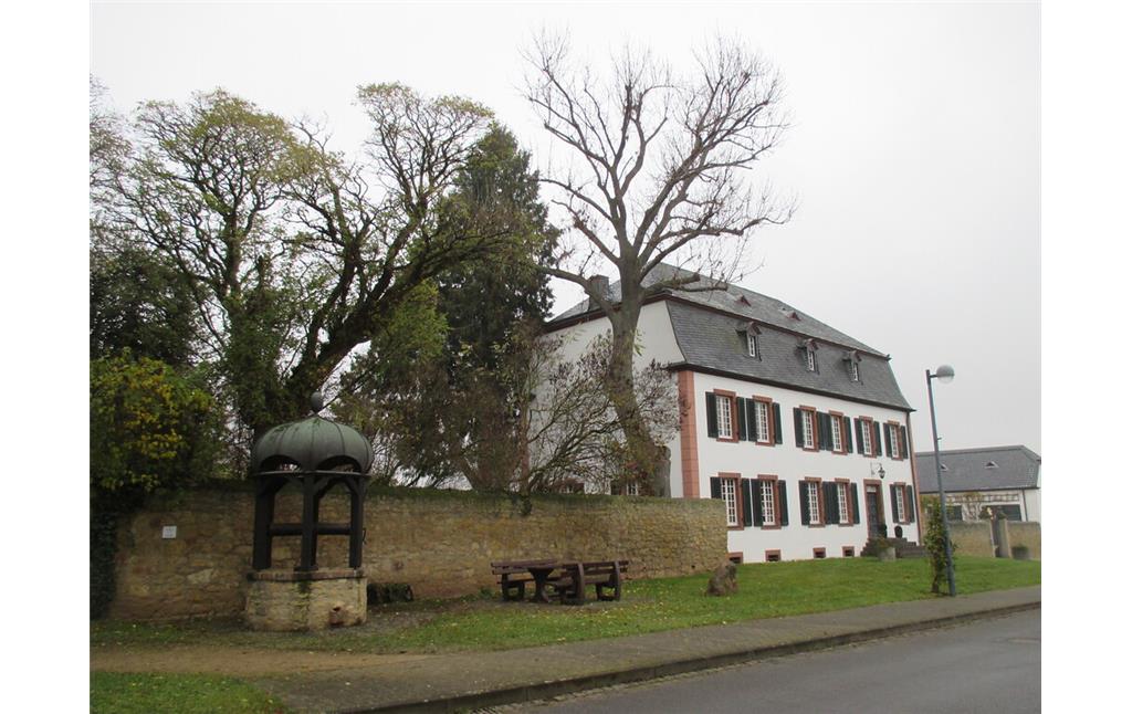 Haus Piedmont in Bürvenich mit Parkanlage und in den 1970er Jahren wiederaufgebautem historischem Dorfbrunnen (2014)