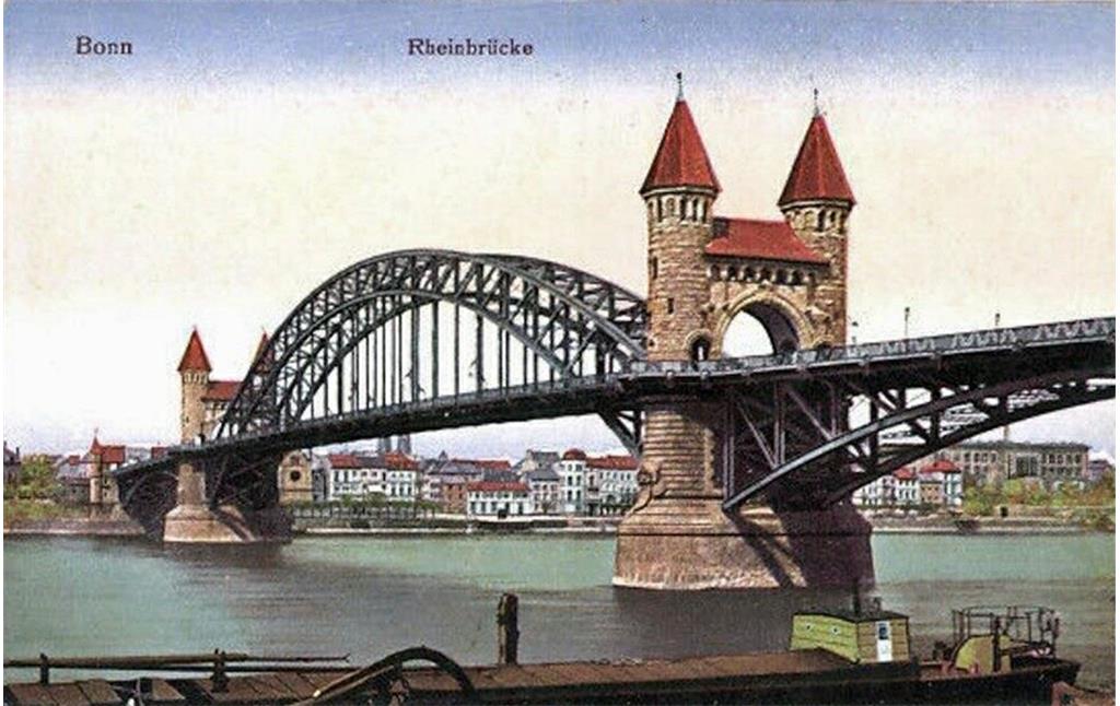 Die auf das Jahr 1900 datierte Farbpostkarte "Bonn, Rheinbrücke" zeigt die Alte Rheinbrücke vom Beueler Flussufer aus. Unter dem zentralen Brückenabschnitt ist am Bonner Rheinufer die Alte Synagoge und daneben das Hotel Dissmann zu erkennen.