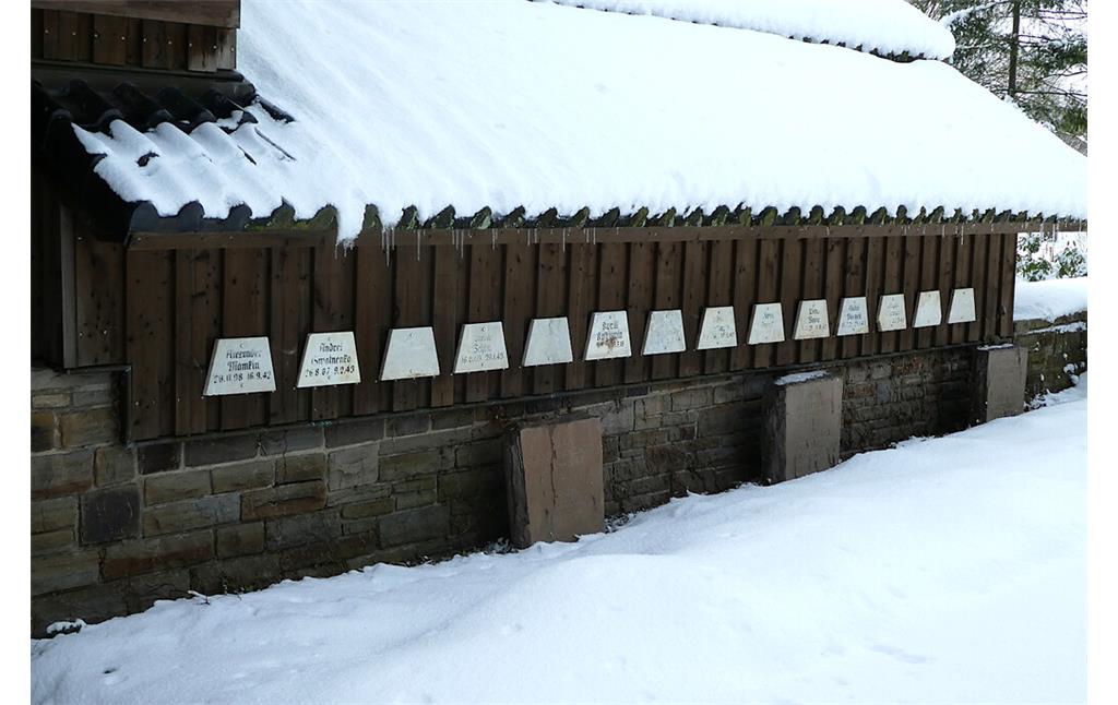 Bild 19: Die 14 Marmortafeln stammen vom Waldfriedhof Eschweiler und wurden 2015 auf der Gräberstätte Rurberg auf der Rückseite des Mehrzweckgebäudes angebracht. 13 der auf den Tafeln genannten Personen sind hier bestattet (2021).