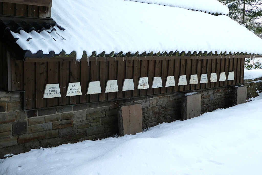 Bild 19: Die 14 Marmortafeln stammen vom Waldfriedhof Eschweiler und wurden 2015 auf der Gräberstätte Rurberg auf der Rückseite des Mehrzweckgebäudes angebracht. 13 der auf den Tafeln genannten Personen sind hier bestattet (2021).