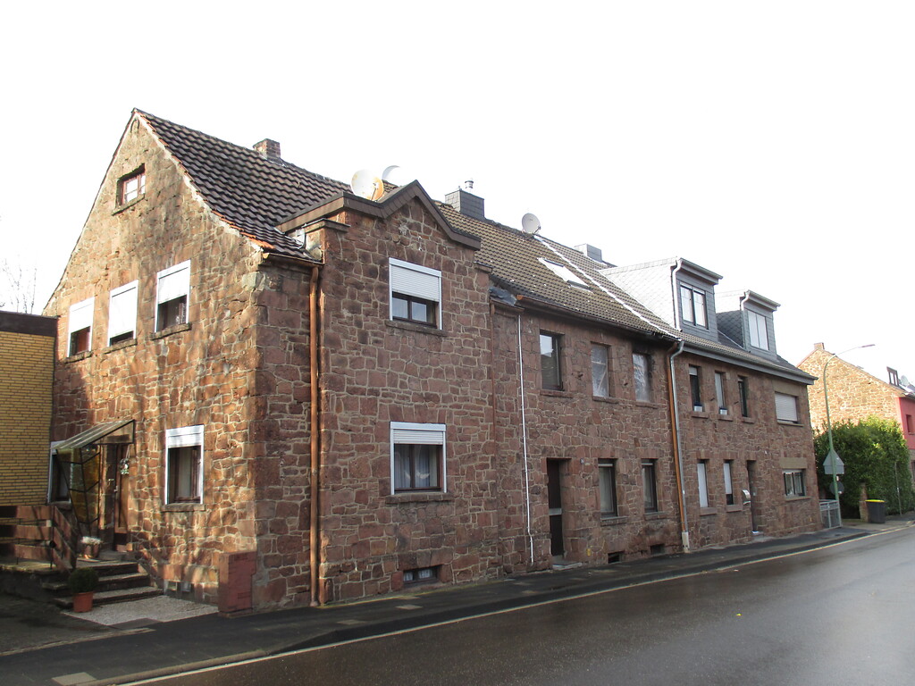In dieser Häuserzeile in Üdingen sind drei traufseitige Häuser aus Bruchstein aneinander gebaut, eines davon weist einen Risalit mit kleinem Giebel auf. (2015)
