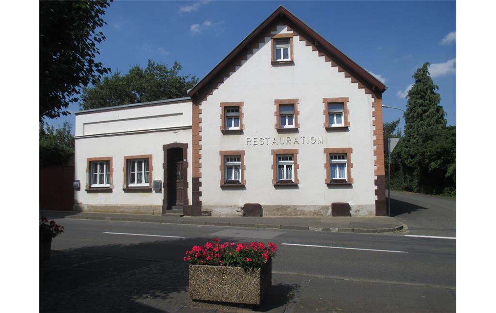 giebelständige ehemalige Restauration mit in rotem Sandstein eingefassten, regelmäßig angeordneten Fenstern und Anbau mit Pultdach in Embken (2015)