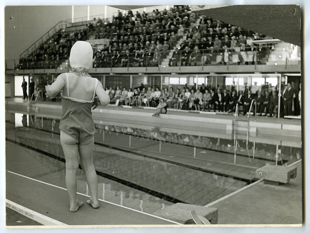 Ein Mädchen in Badebekleidung auf dem Sprungbrett im Bonner Frankenbad, im Hintergrund volle Zuschauertribünen (1963)