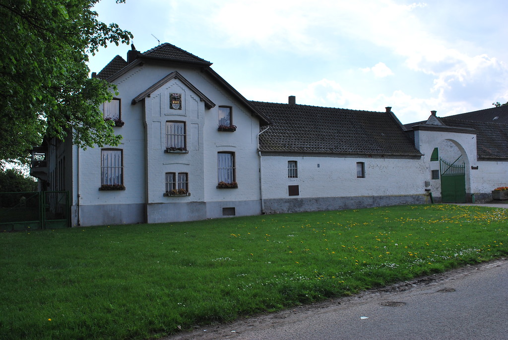 Der Fronhof ist eine repräsentative, geschlossene Hofanlage aus weiß geschlämmtem Backstein. Hier zu sehen ist die Ansicht von der Fronhofstraße mit der Toreinfahrt und dem Wohnhaus mit vorgesetztem Risalit an der Giebelseite. Der Hof ist von einem breiten Rasenstreifen umgeben (2014).