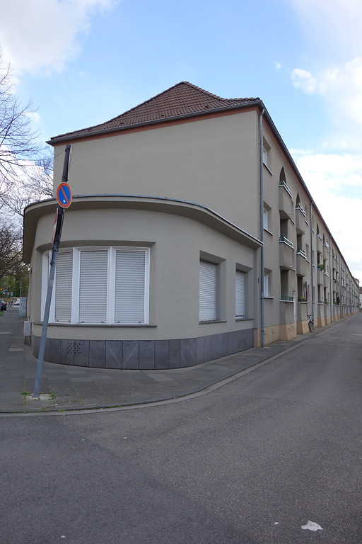Gestaltung einer Straßenecke in der Siedlung Grüner Hof. Ein eingeschossiger Halbrundbau, der durch Fenster gegliedert ist, schließt die Häuserzeile an der Straßenecke ab (2016).